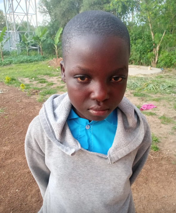 A young Black child in gray hoodie and blue shirt, looking somber outdoors.