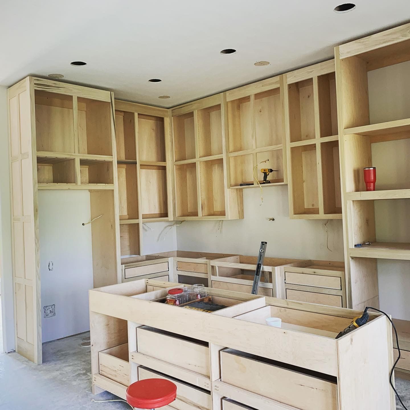 Unfinished kitchen with bare wood cabinets, white island, and built-in shelves under construction.