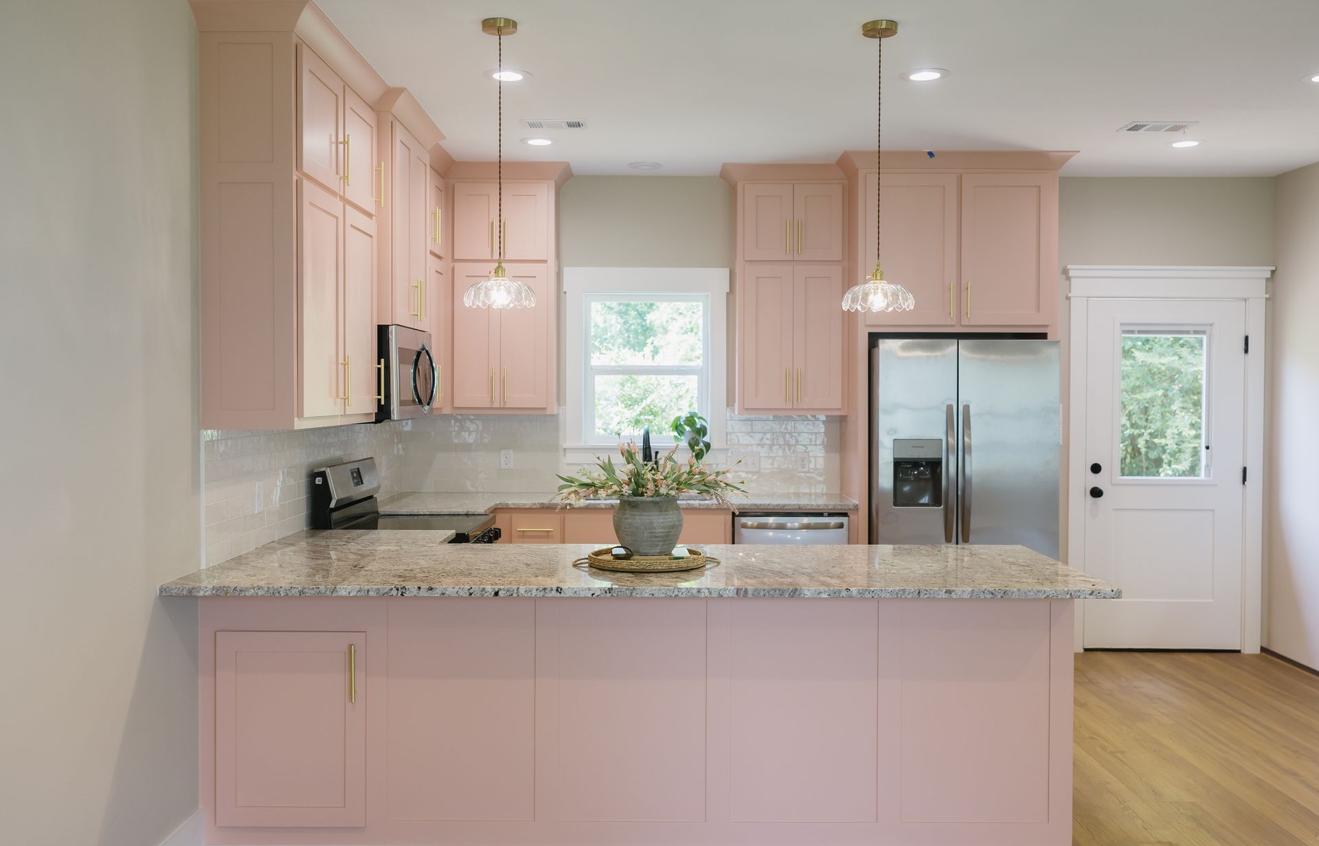 Bright kitchen with pink cabinets, granite island, stainless appliances, and hardwood floors.