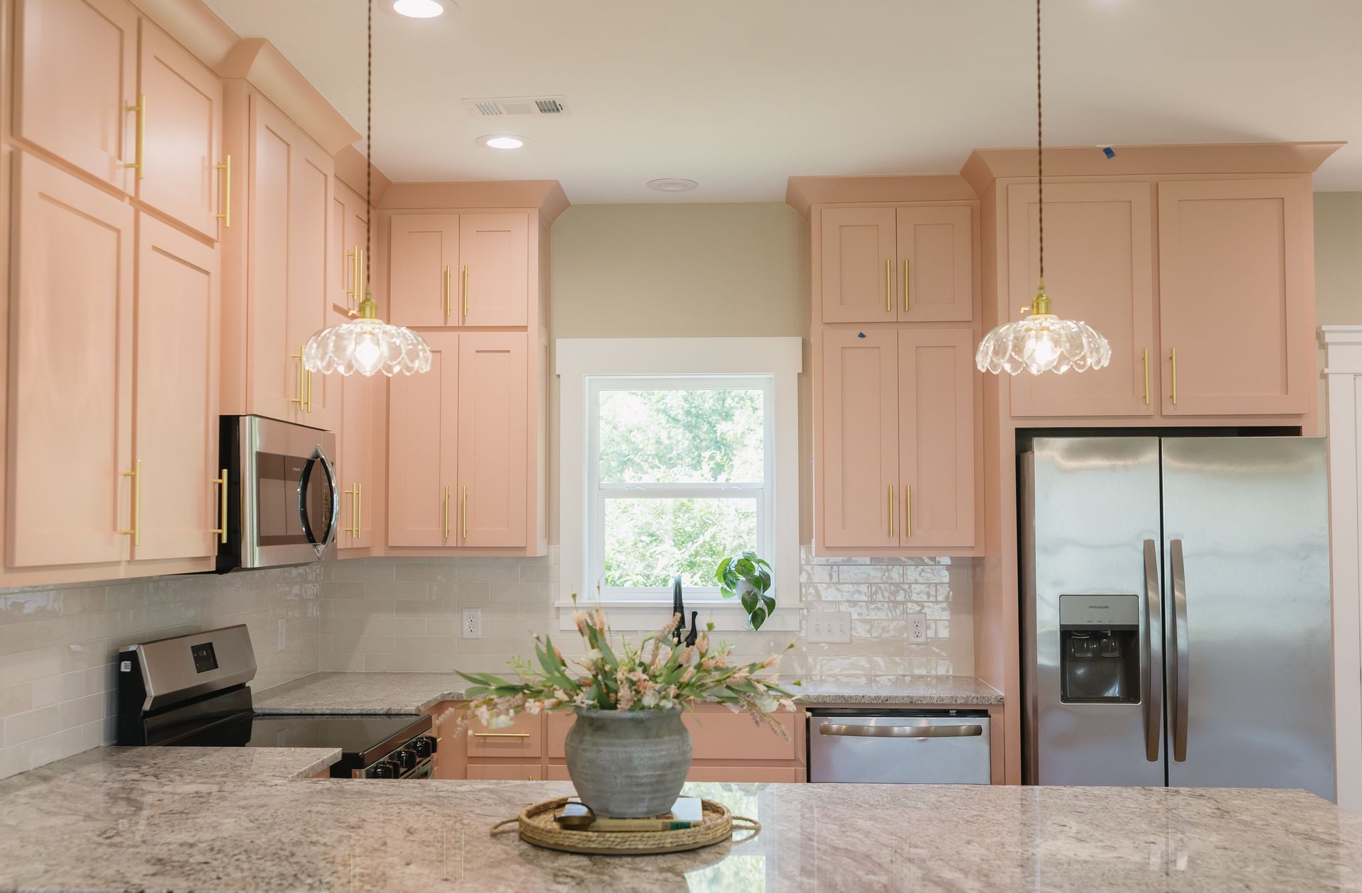 Bright kitchen with light pink cabinets, granite island, stainless fridge, and pendant lights.