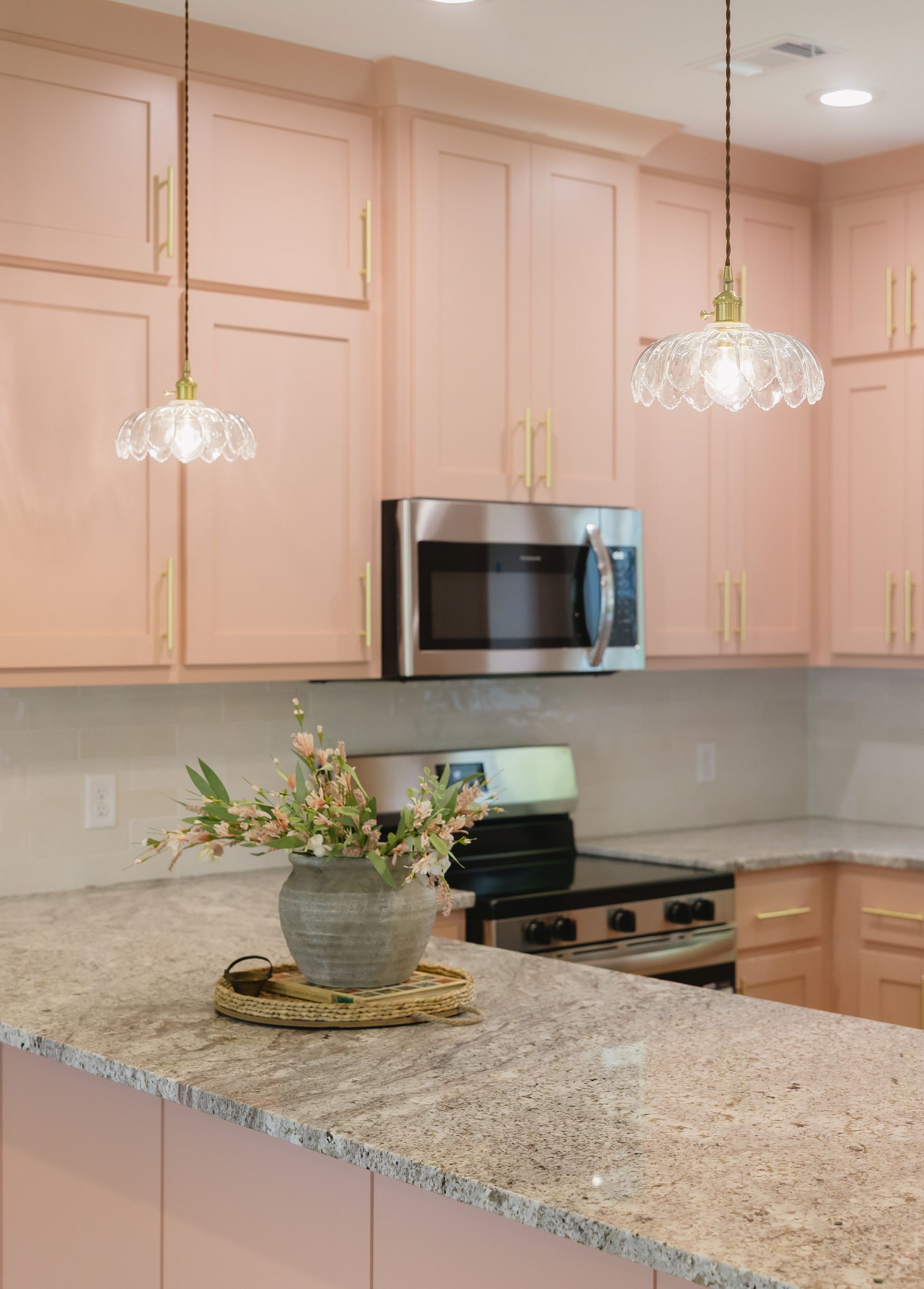Bright kitchen with pale cabinets, granite island, stainless microwave, and two pendant lights