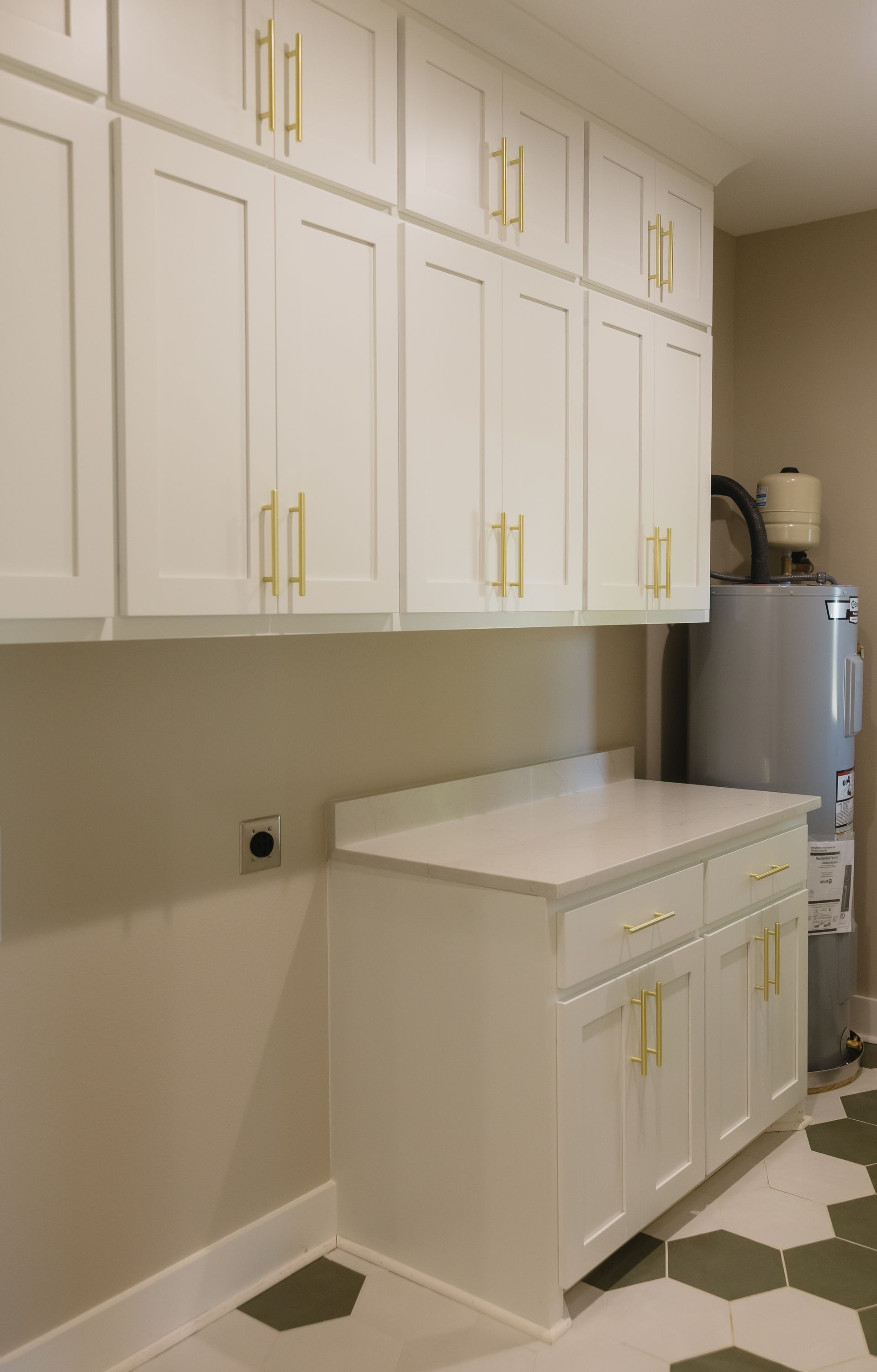 Laundry room with white cabinets, countertop, water heater, and patterned tile floor.