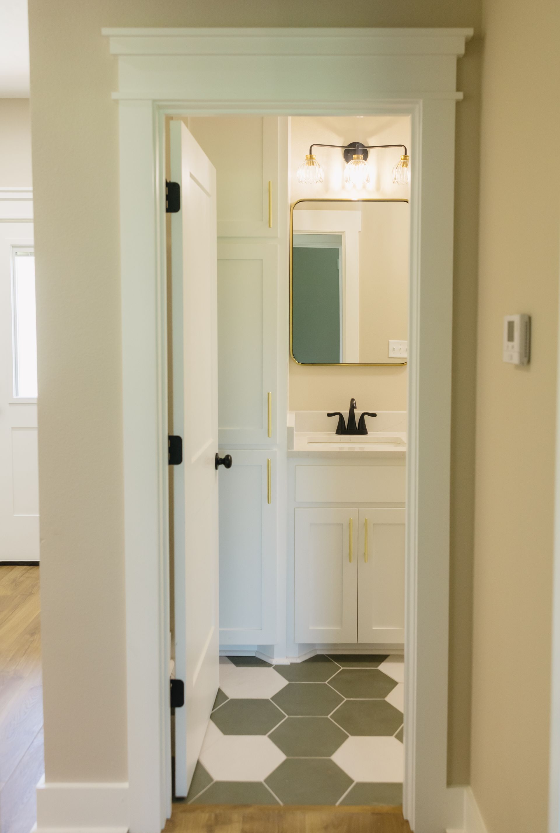 Hallway view into a small bathroom with white vanity, mirror, and green hexagon floor tiles