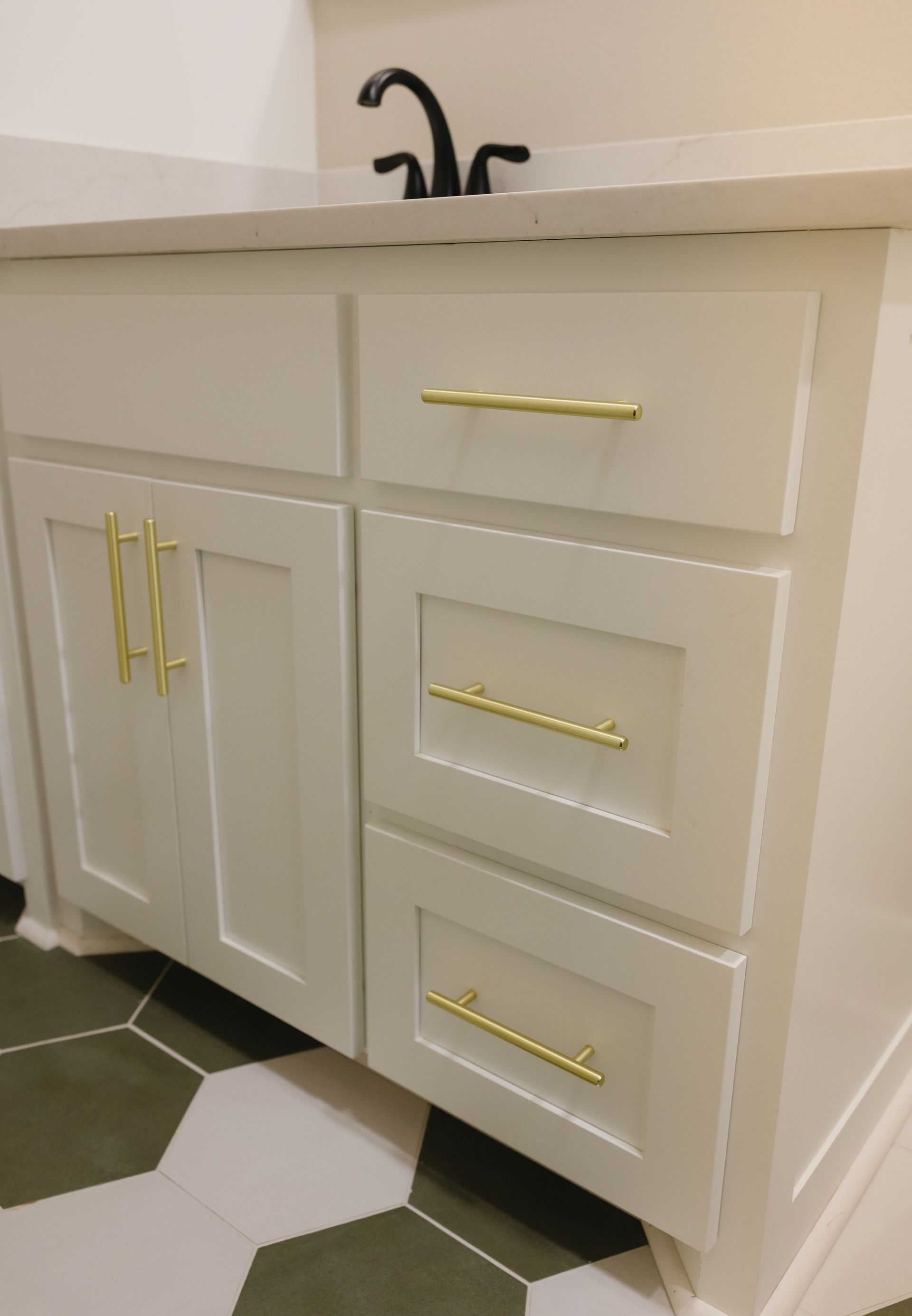 White bathroom vanity with gold handles, black faucet, and hexagonal black-and-white tile floor.
