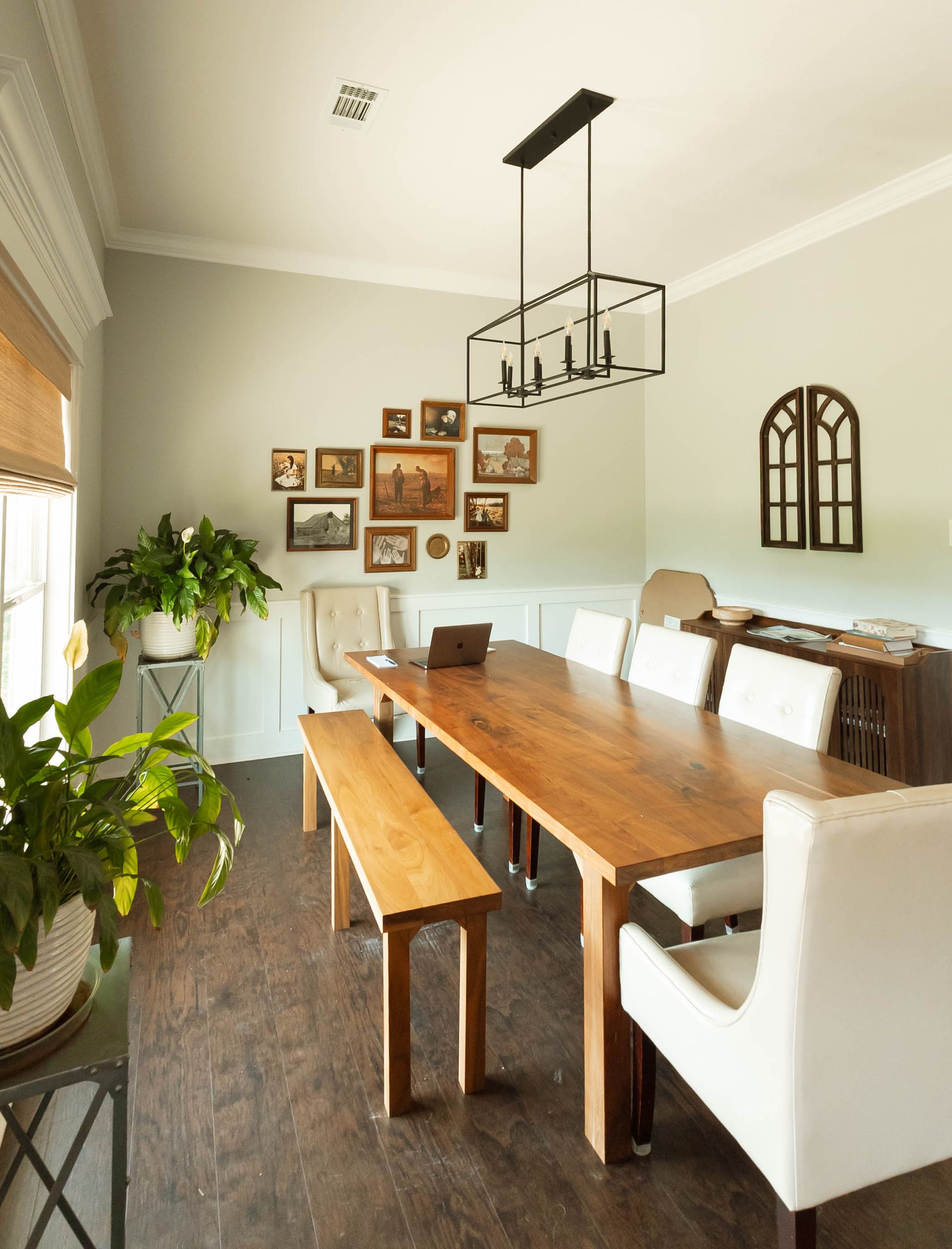 Bright dining room with wooden table, white chairs, bench, hanging light, and wall art