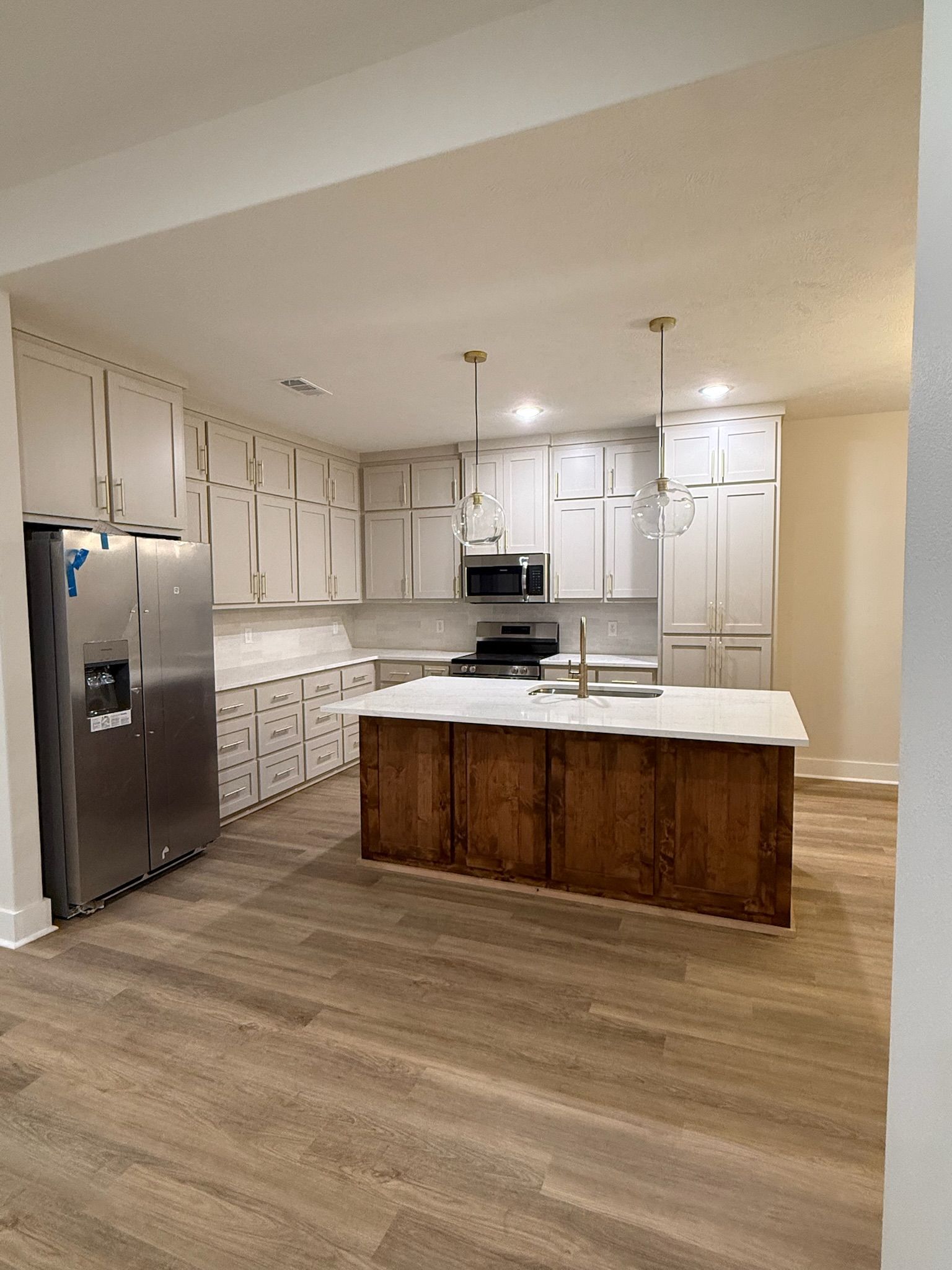 Modern kitchen with white cabinets, stainless fridge, marble island, and wood-look flooring