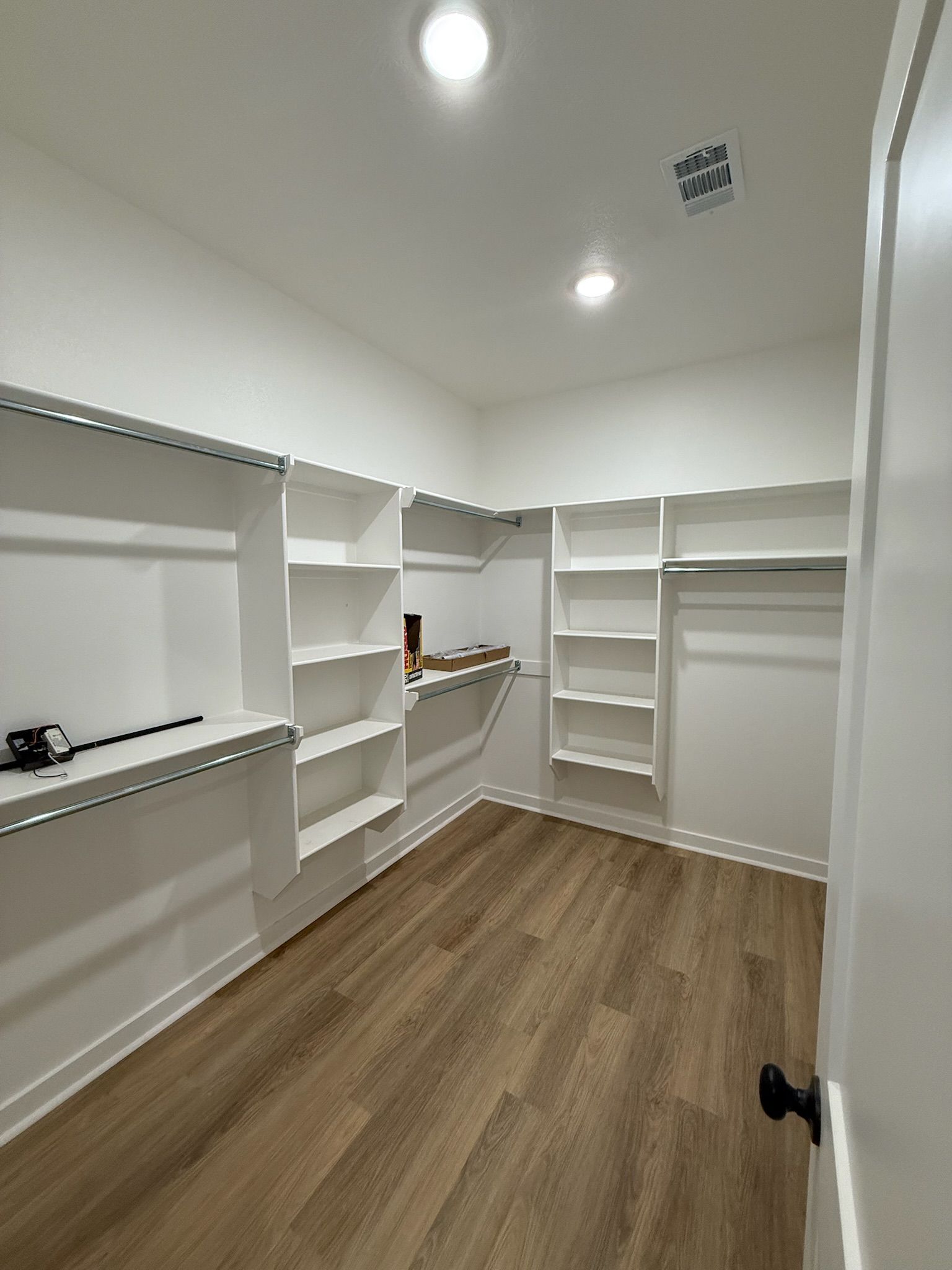 Empty white walk-in closet with built-in shelves and hanging rods, wood-look floor, and recessed ceiling lights