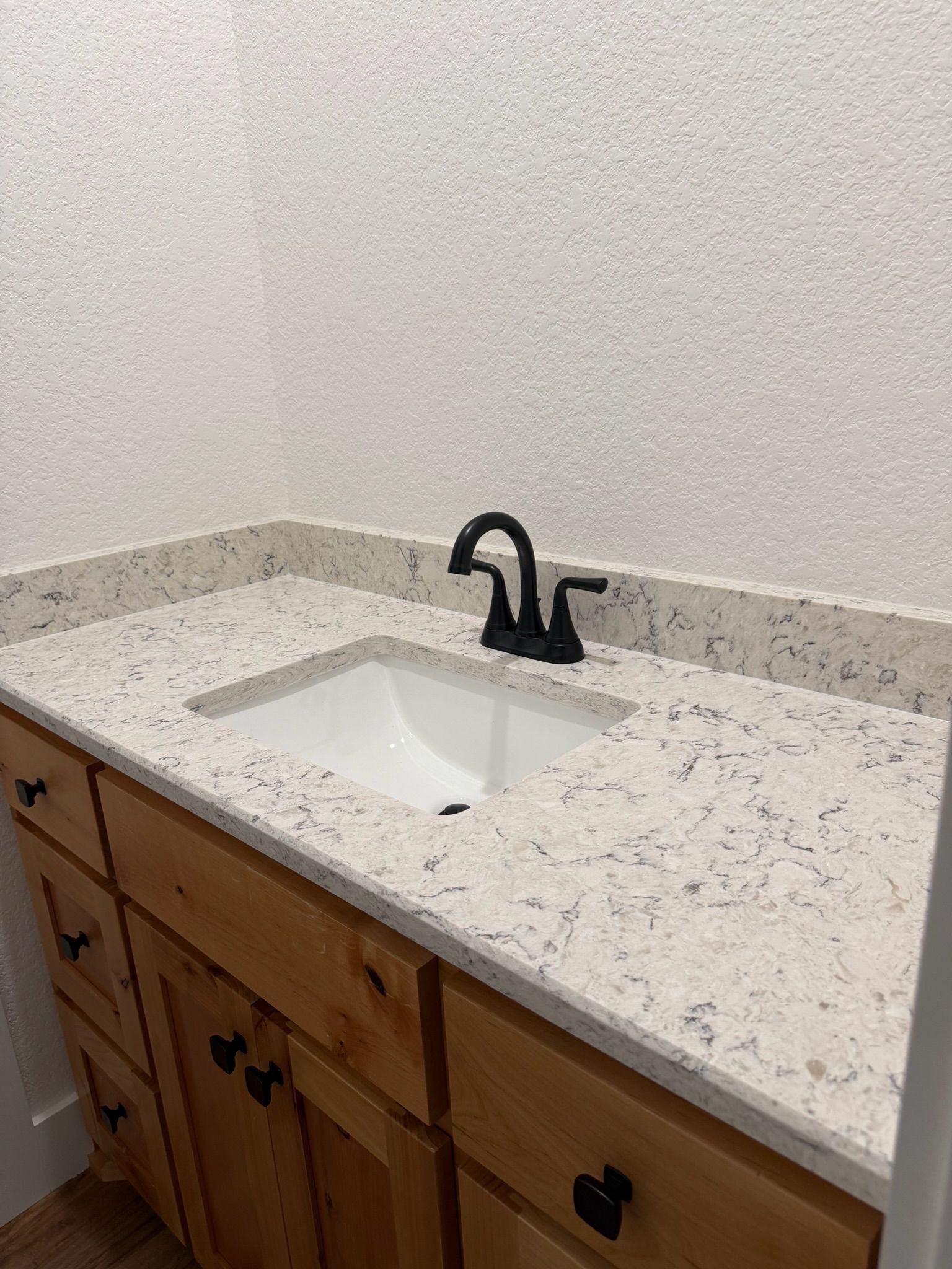 Bathroom vanity with speckled countertop, white sink, and black faucet against a white wall