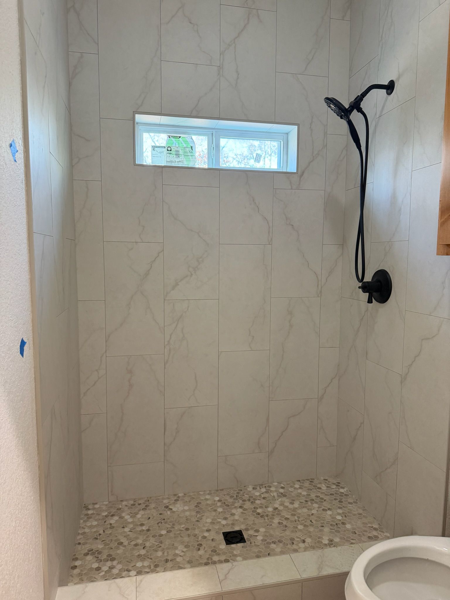 Small tiled shower stall with a pebble floor, narrow window, and exposed plumbing fixture.