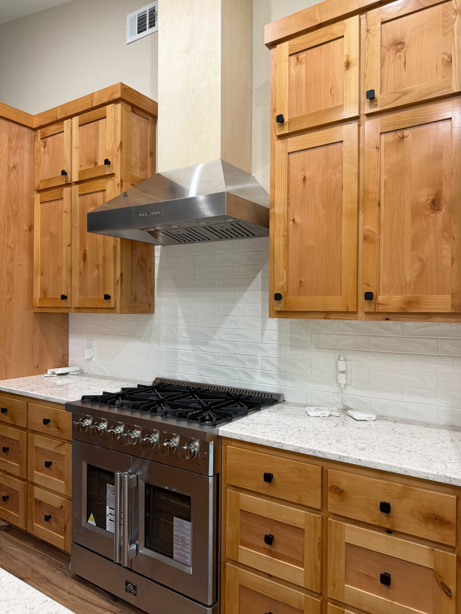 Modern kitchen with wood cabinets, stainless steel range hood, gas stove, and marble backsplash