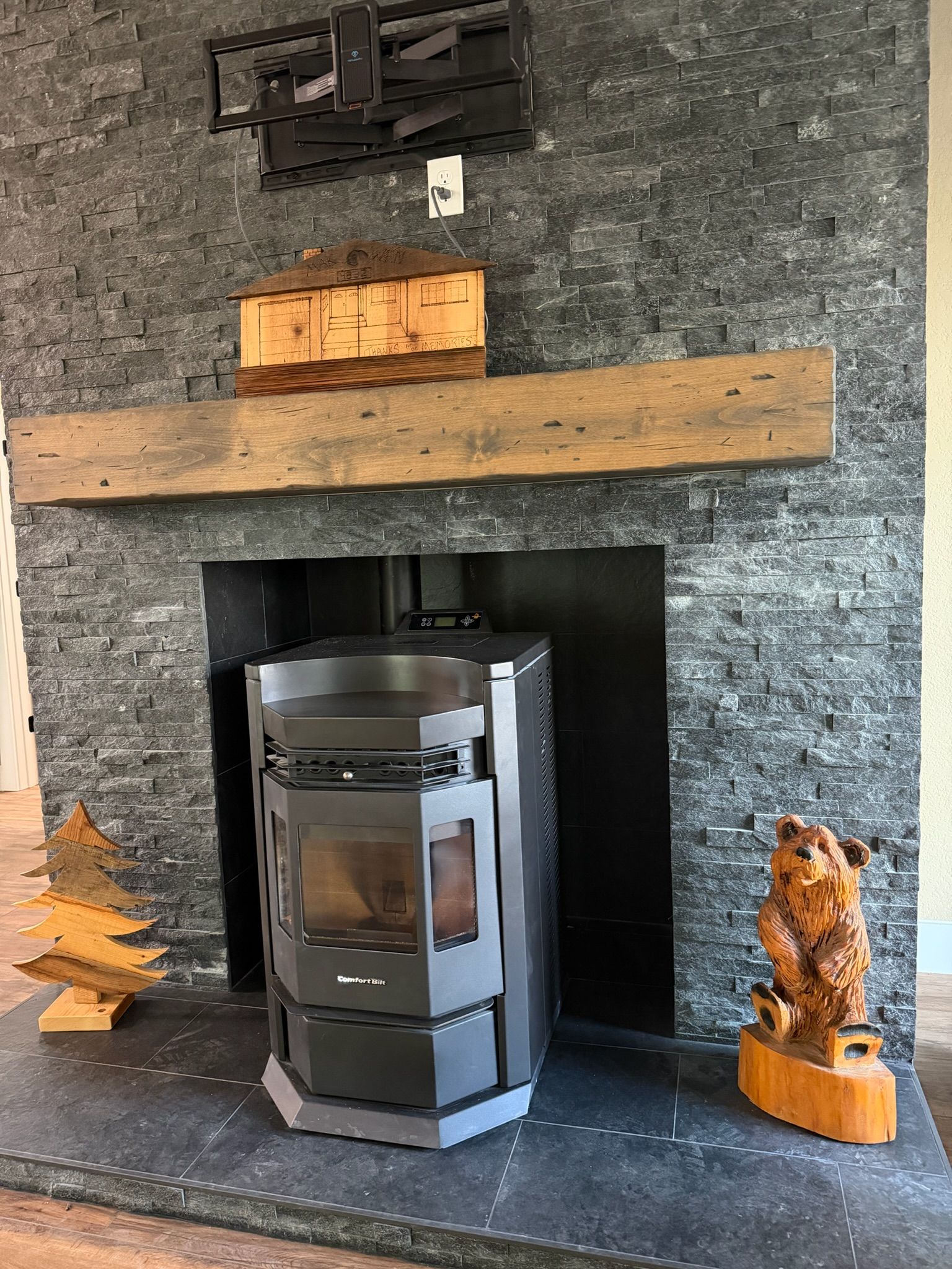 Stone fireplace with a wood mantel and small sculptures, centered around a black stove in a living room.