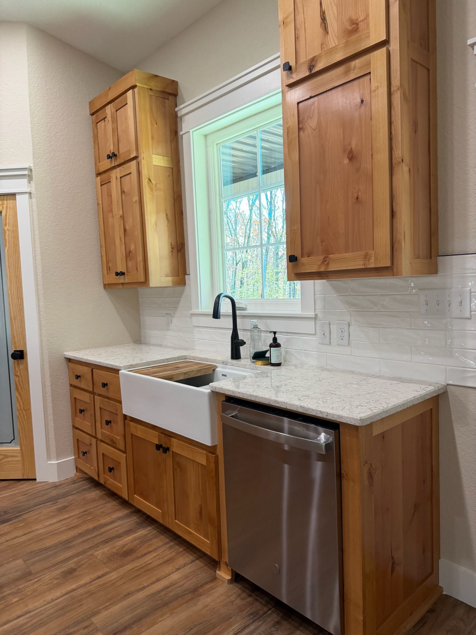 Modern kitchen with wood cabinets, white tile backsplash, farmhouse sink, and stainless dishwasher.