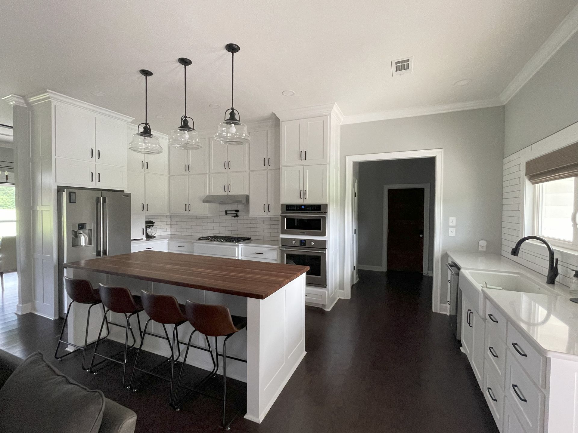 Modern white kitchen with island, wood countertop, pendant lights, stainless appliances, and dark flooring