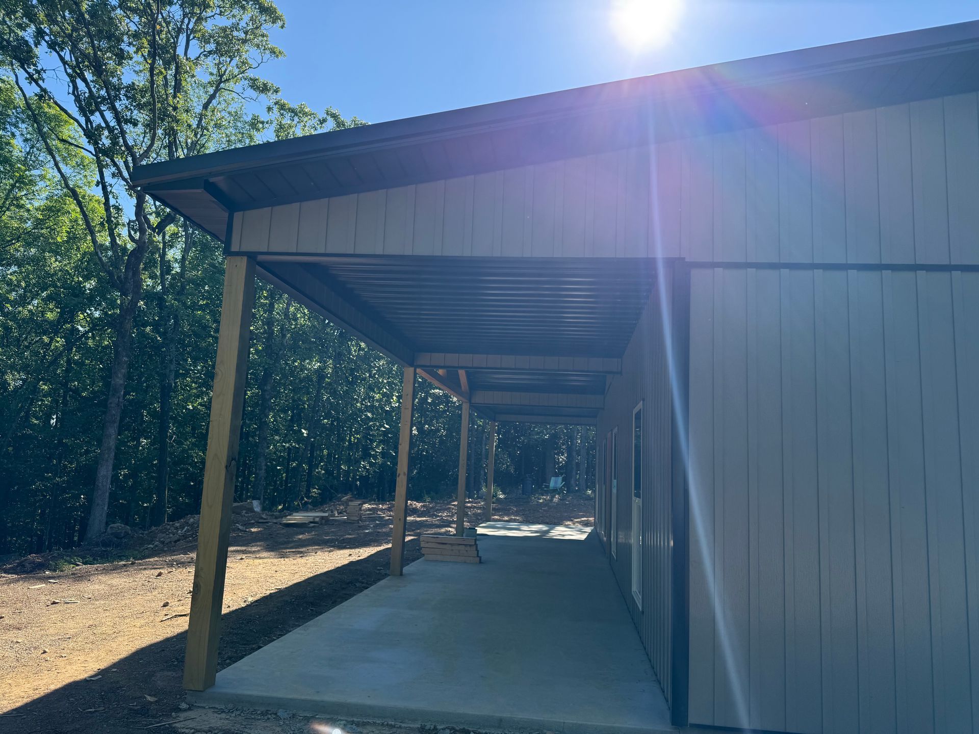 Covered outdoor walkway beside a building, with metal posts and sunlit trees in the background