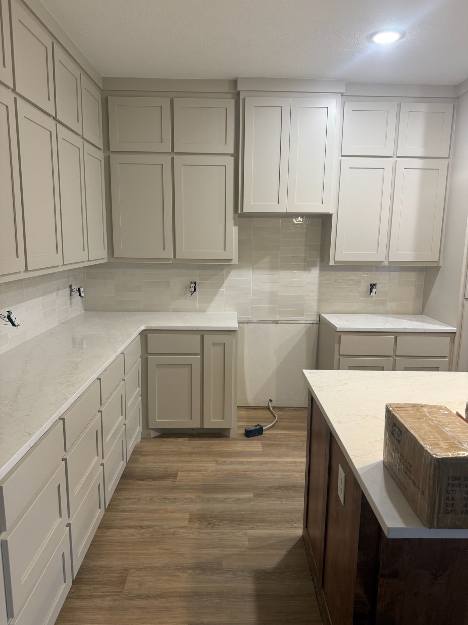 Bright modern kitchen with white cabinets, light counters, wood floor, and an island in the foreground