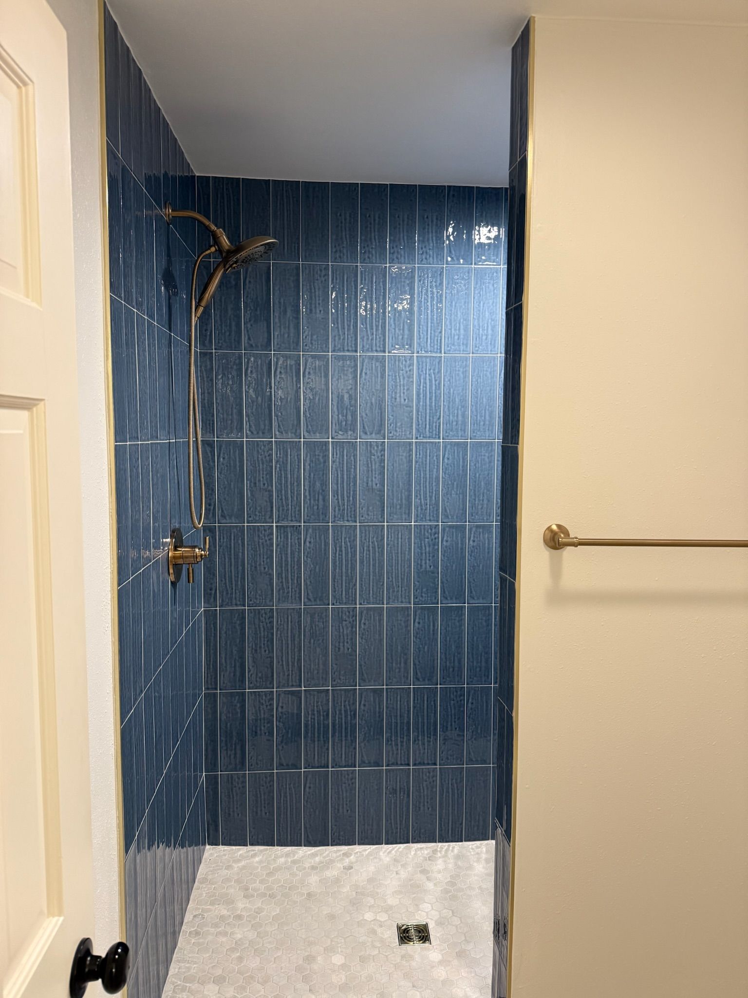 Small bathroom with blue tiled shower area, white floor, and beige walls.