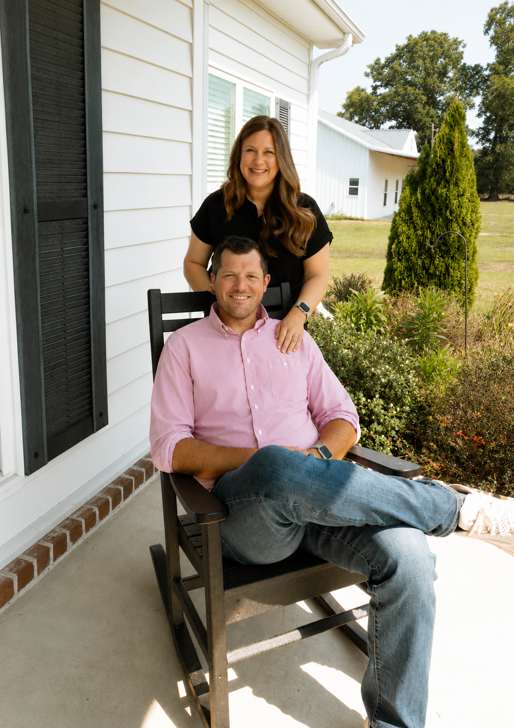 Couple seated on a porch chair outside a white house, smiling and relaxing