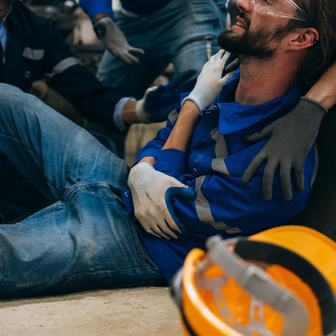 Injured man in blue shirt being held by rescuers, with helmet in foreground