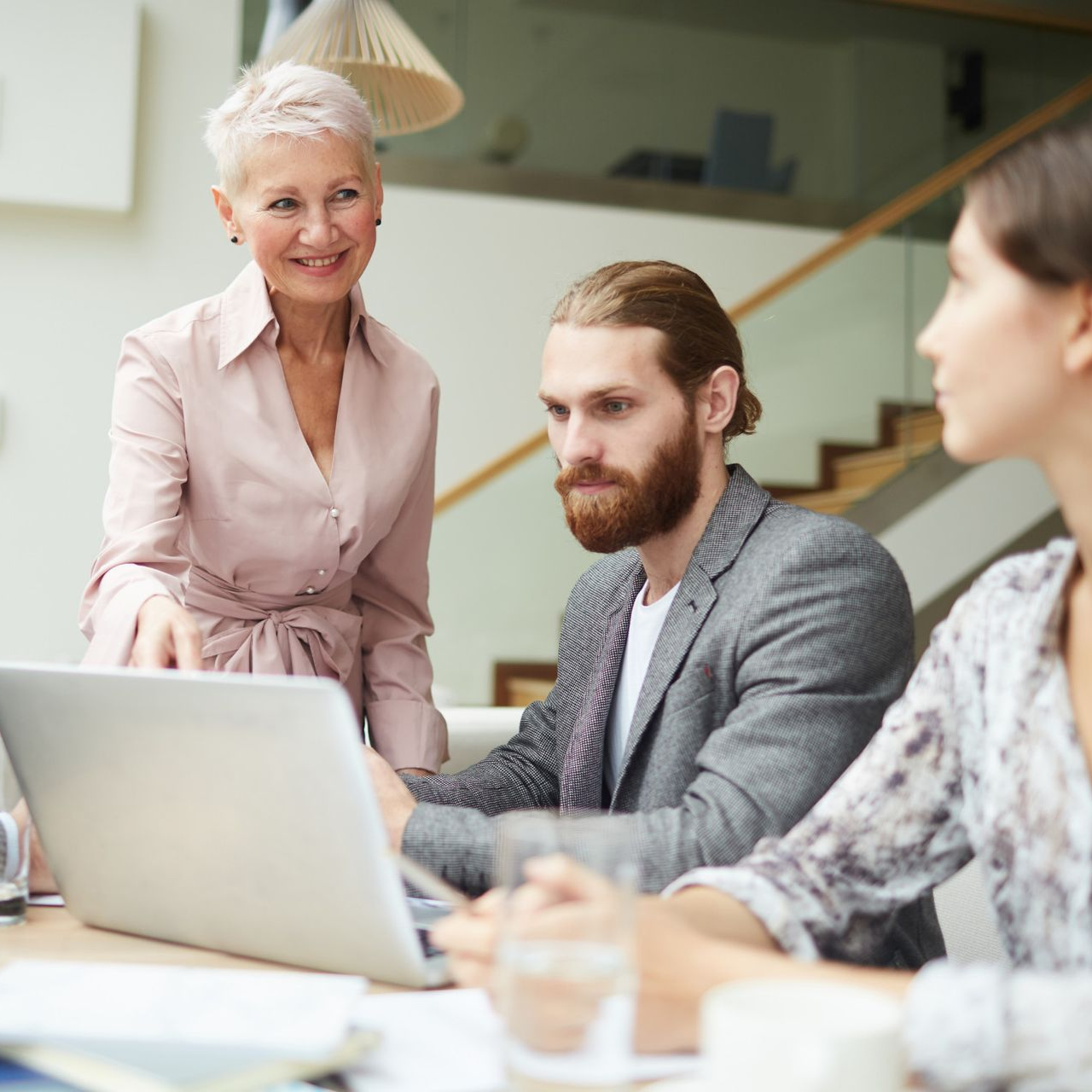 Colleagues in a meeting around a laptop, with one woman standing and speaking nearby