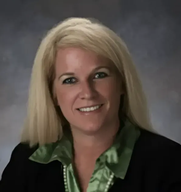 Studio headshot of a smiling woman with blonde hair in a black blazer and green blouse