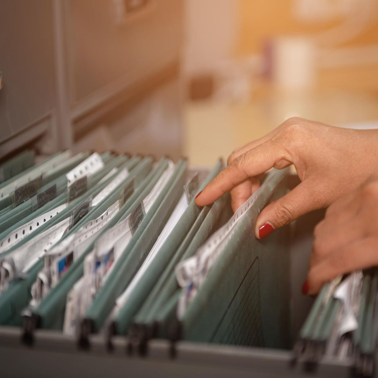 Hand reaching through hanging file folders in a filing cabinet