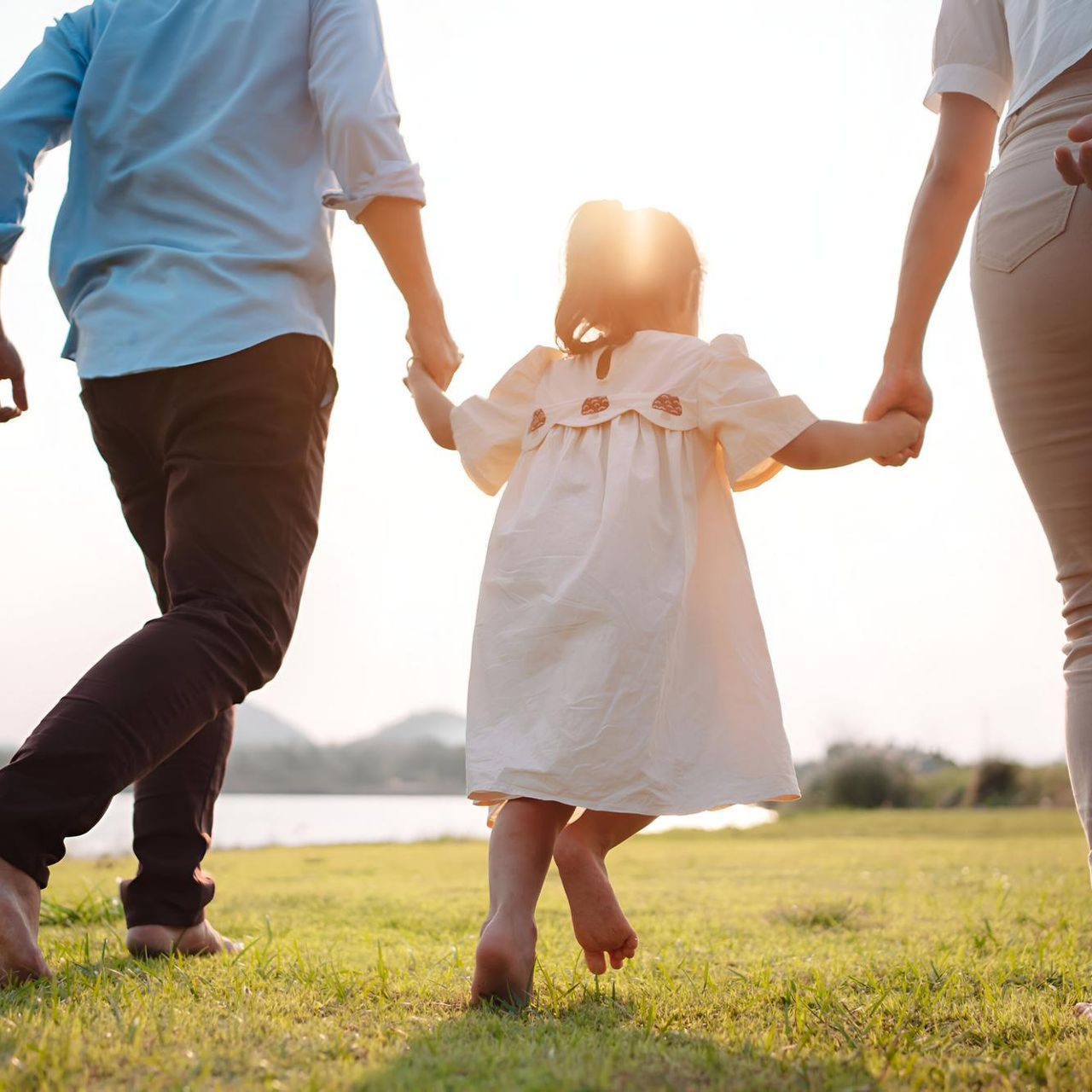 Family holding hands and walking across a sunny grassy field at sunset