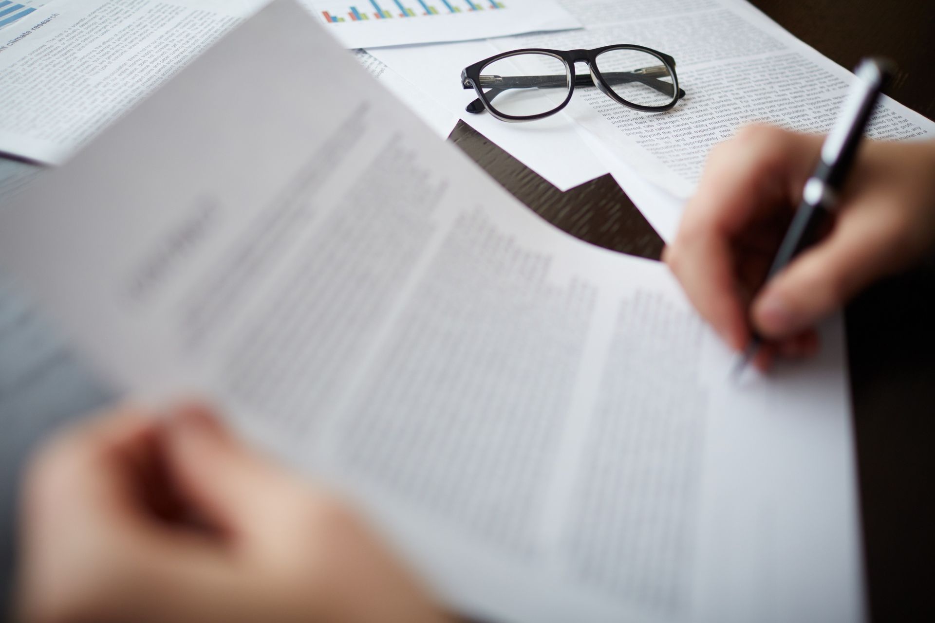 Hands reviewing documents with pen and eyeglasses on a desk