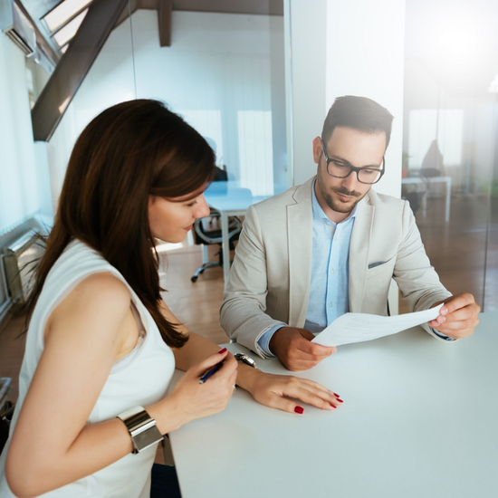 Two colleagues reviewing documents at a desk in a bright office