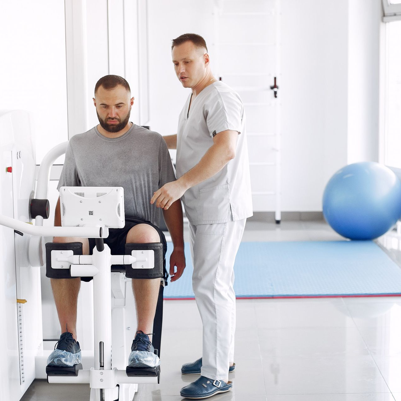 Physical therapist assisting a seated patient with leg exercises in a bright rehab clinic