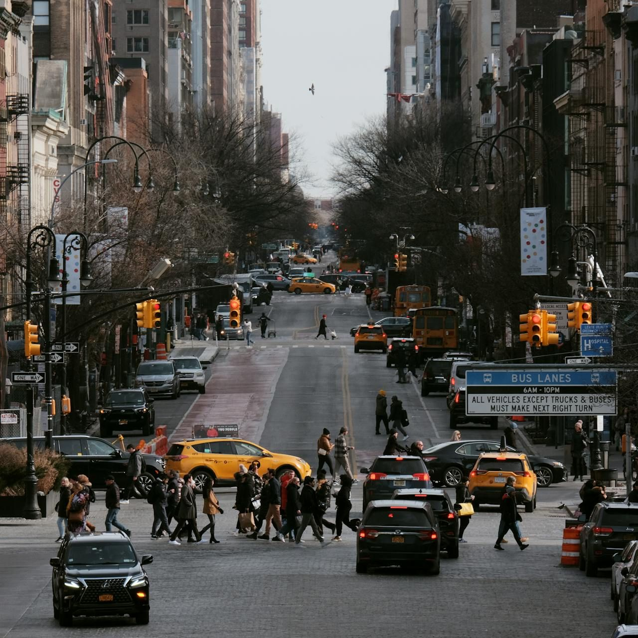 Busy city street with yellow taxis and pedestrians crossing between tall buildings