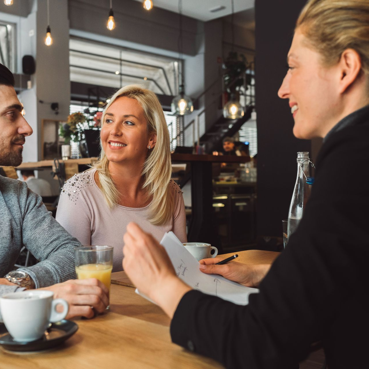 Three people chatting at a café table, smiling over drinks in a warm modern interior