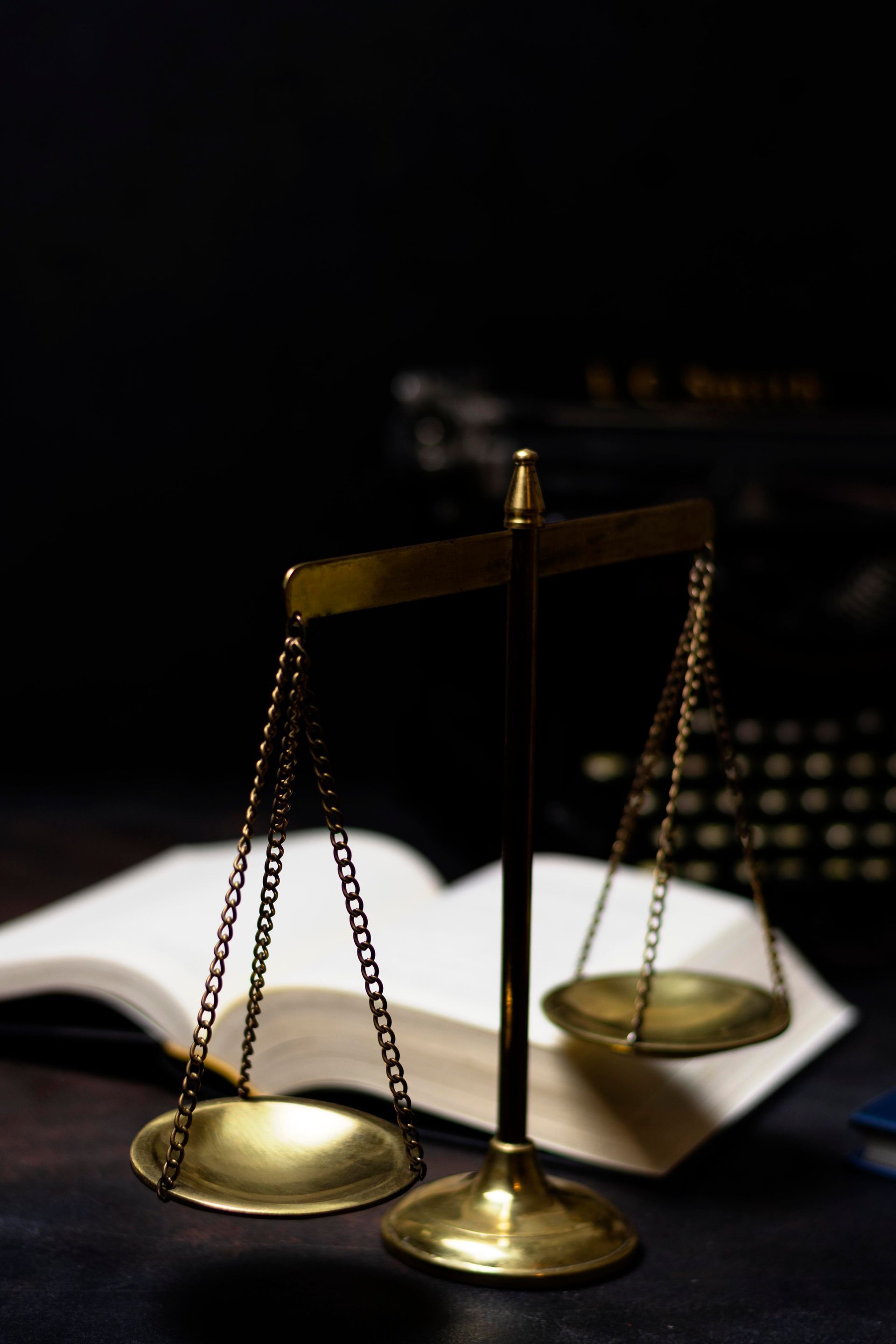 Brass balance scale on open law book, with blurred gavel in the background