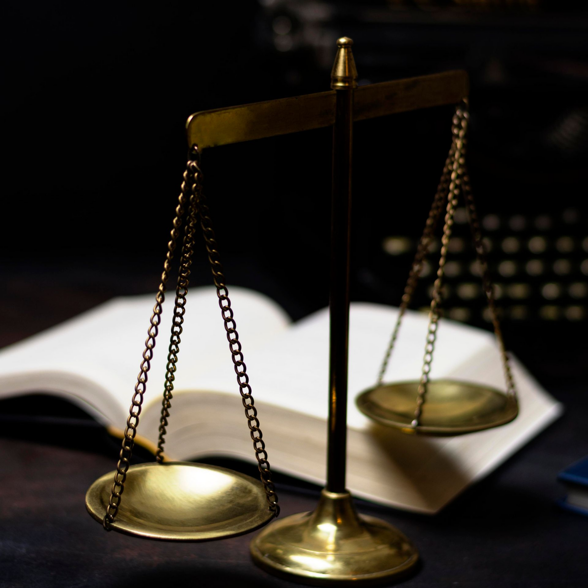 Brass balance scales on a desk beside an open book, symbolizing law and justice