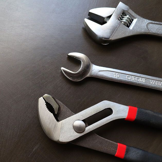 Three metal wrenches on a dark surface: adjustable, open-ended, and slip-joint pliers.