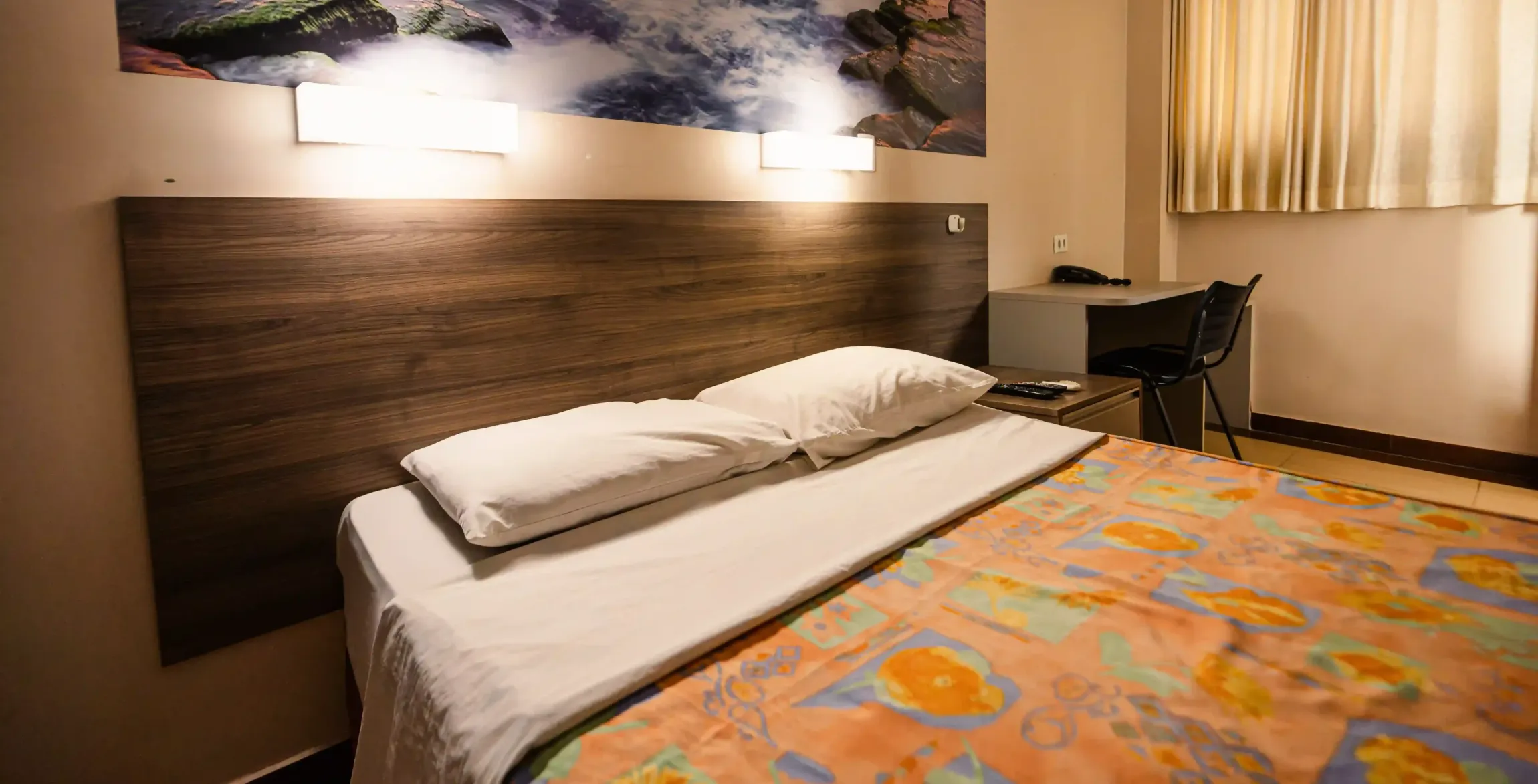Um quarto de hotel com uma cama, escrivaninha, cadeira e uma pintura na parede Oly Plaza Hotel