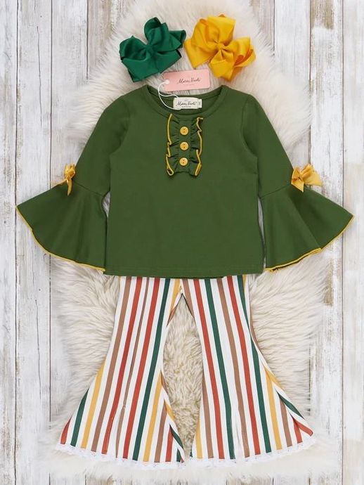 Green bell-sleeve top with gold trim and striped flared pants on a white fur backdrop, accented by yellow and green flowers