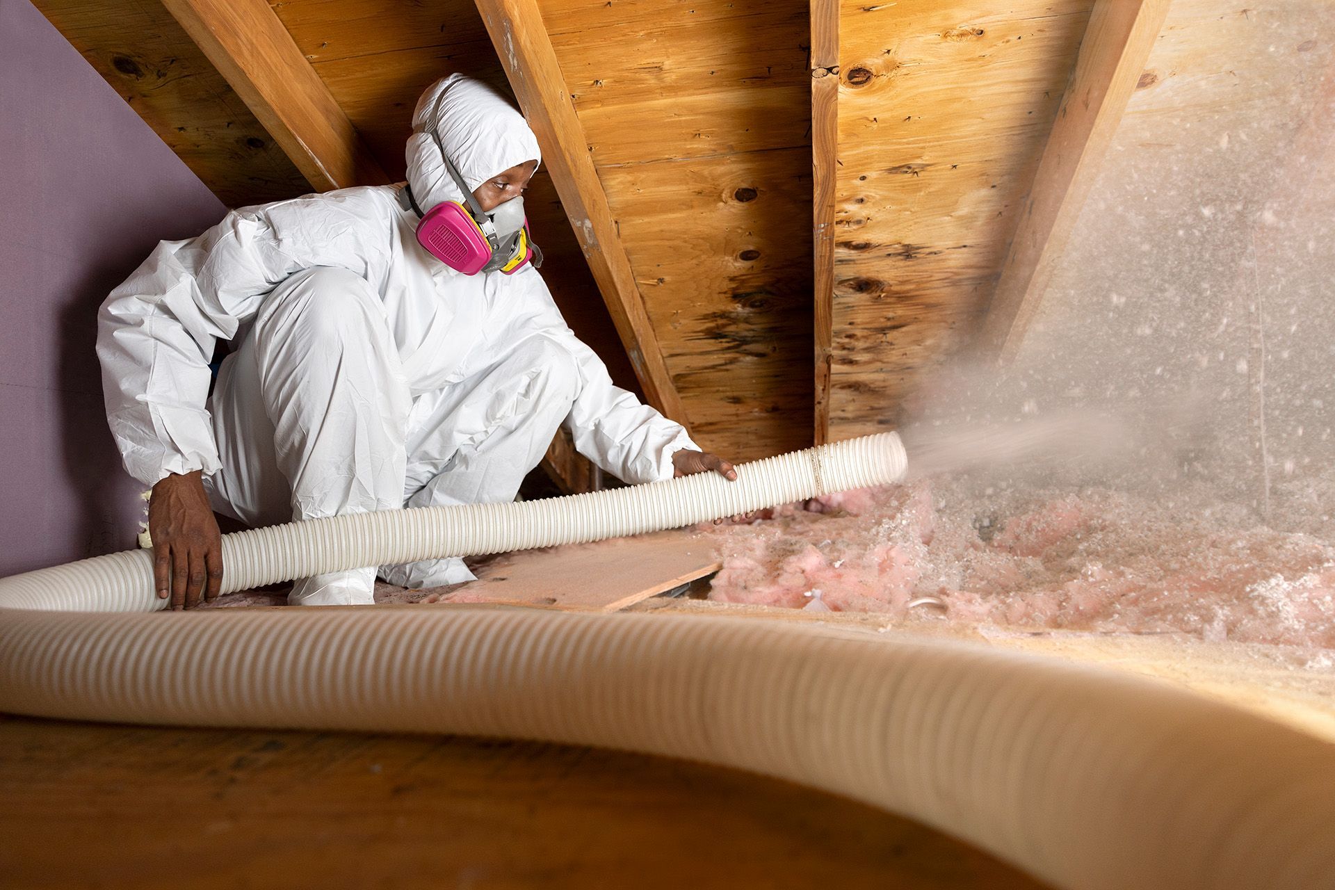 A man in a protective suit is blowing insulation into an attic.