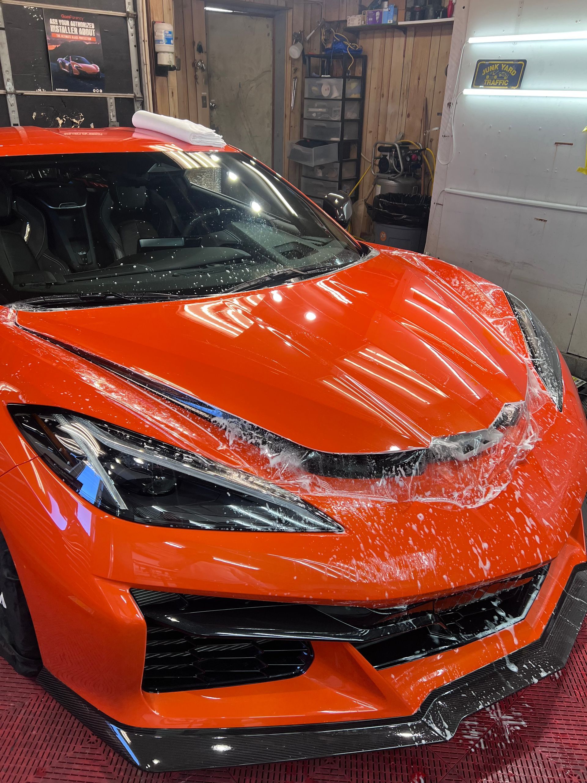 Orange sports car being washed with soapy water; indoors in a garage.