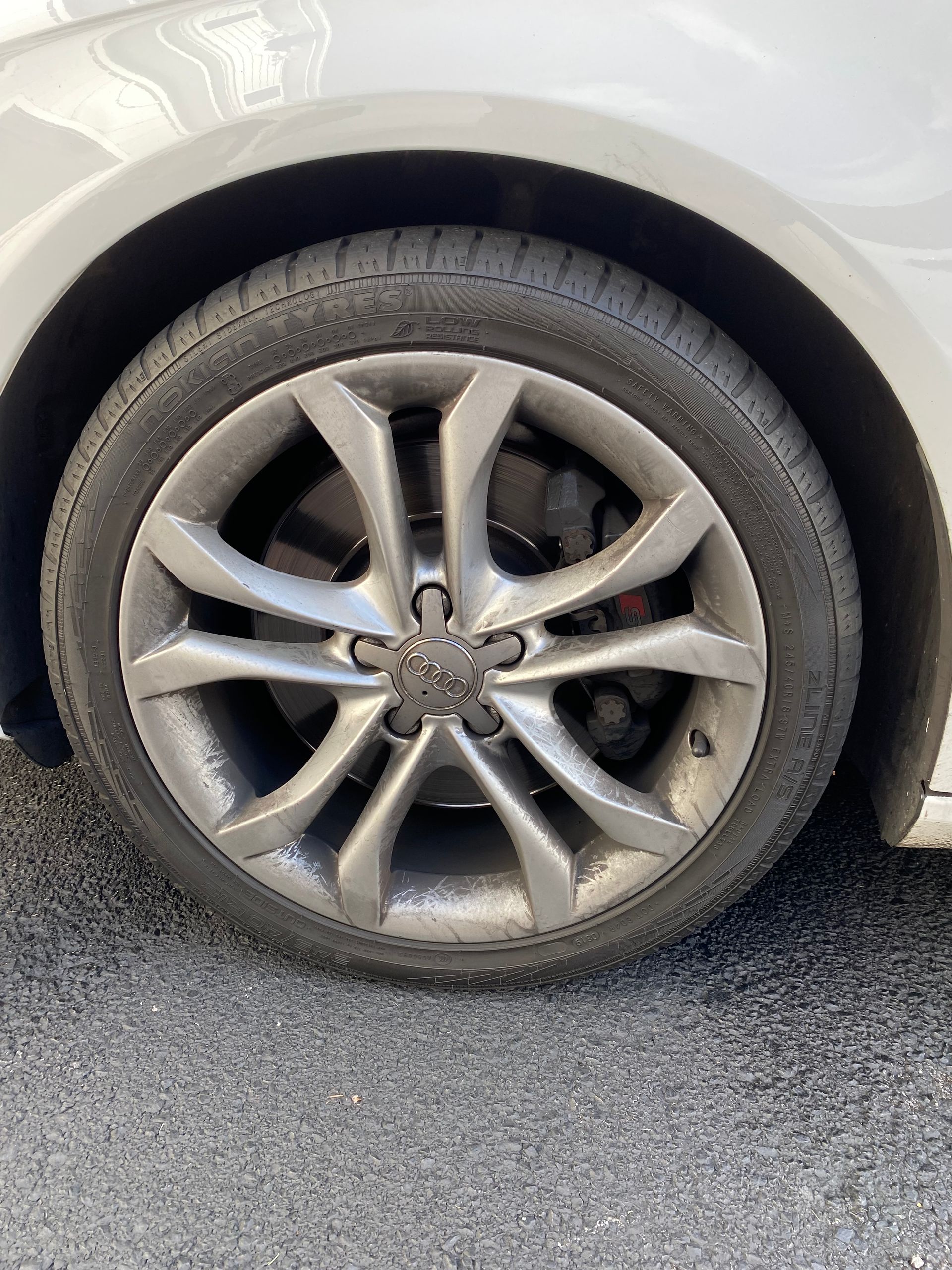 Close-up of a silver Audi wheel and tire on a car parked outside.
