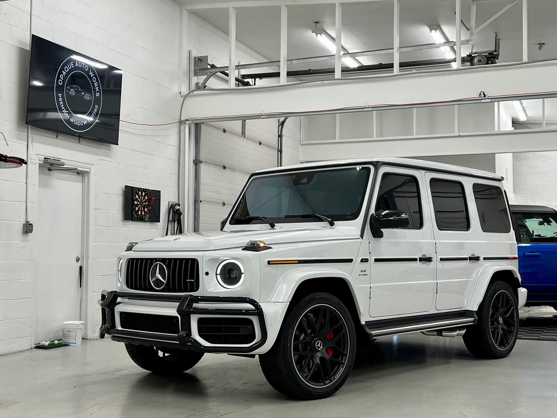 White Mercedes-Benz G-Class SUV parked inside a well-lit garage, with black wheels and tinted windows.