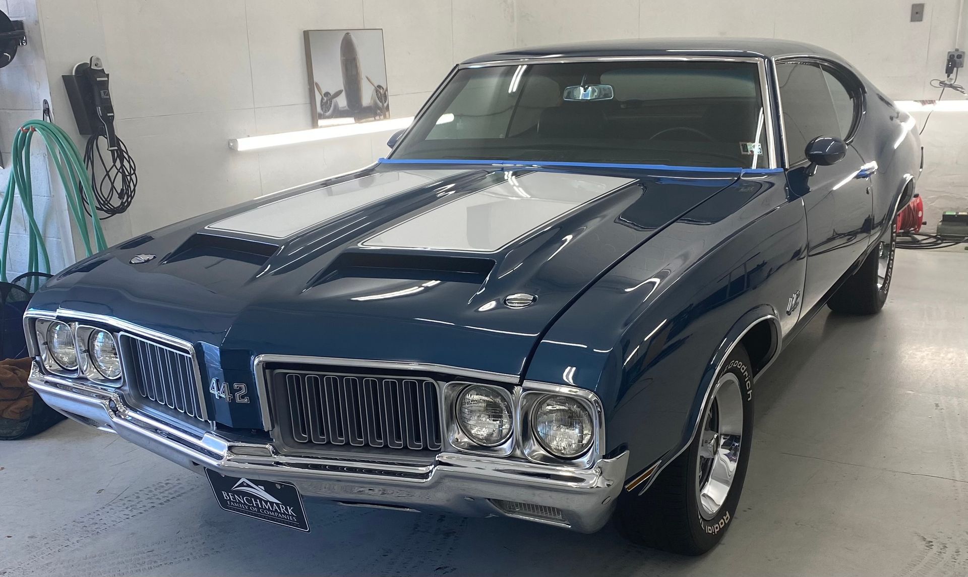 Blue and silver 1970 Oldsmobile 442 muscle car with chrome trim, parked indoors.