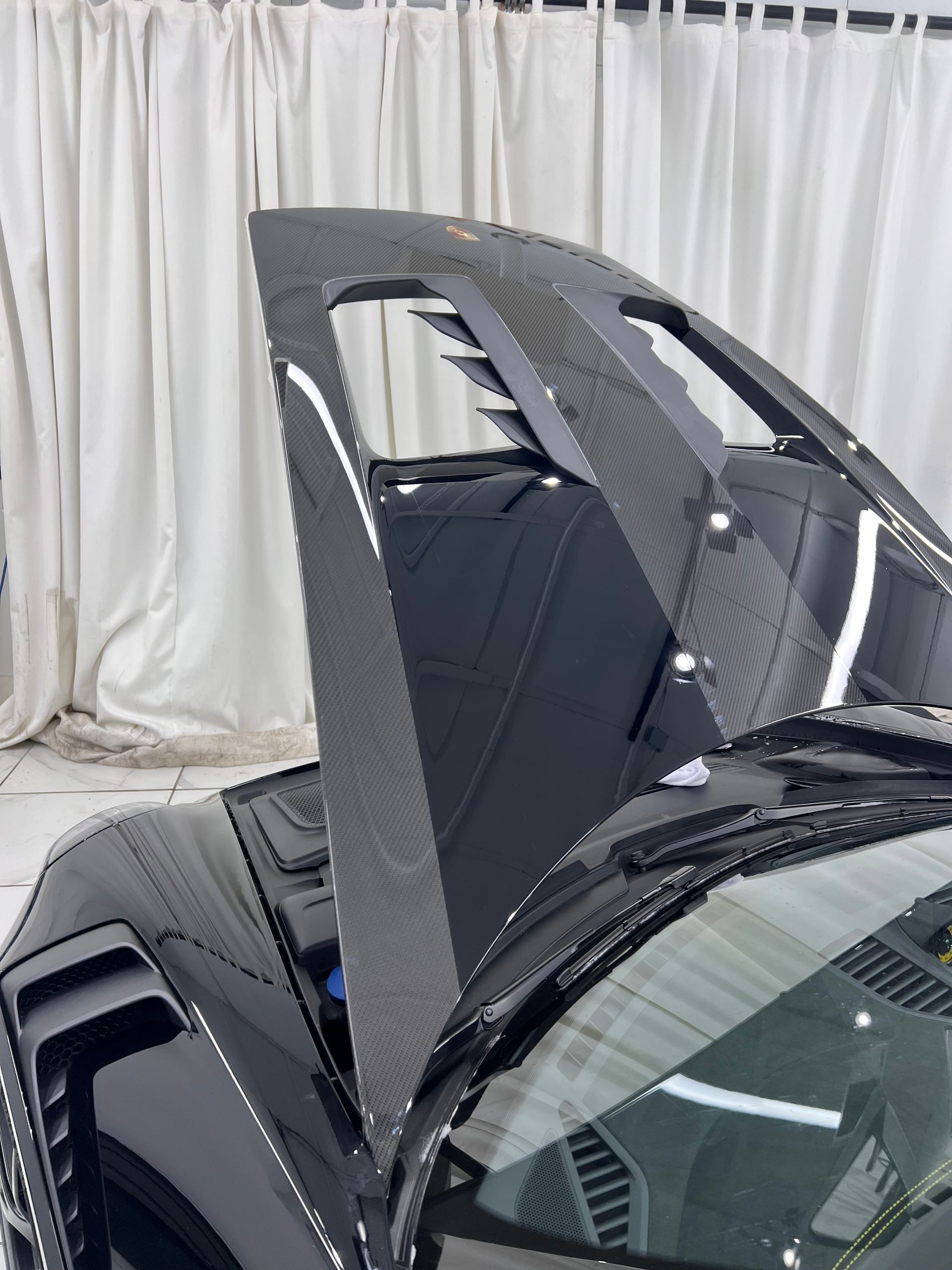 Black sports car hood open, revealing engine bay with carbon fiber accents.
