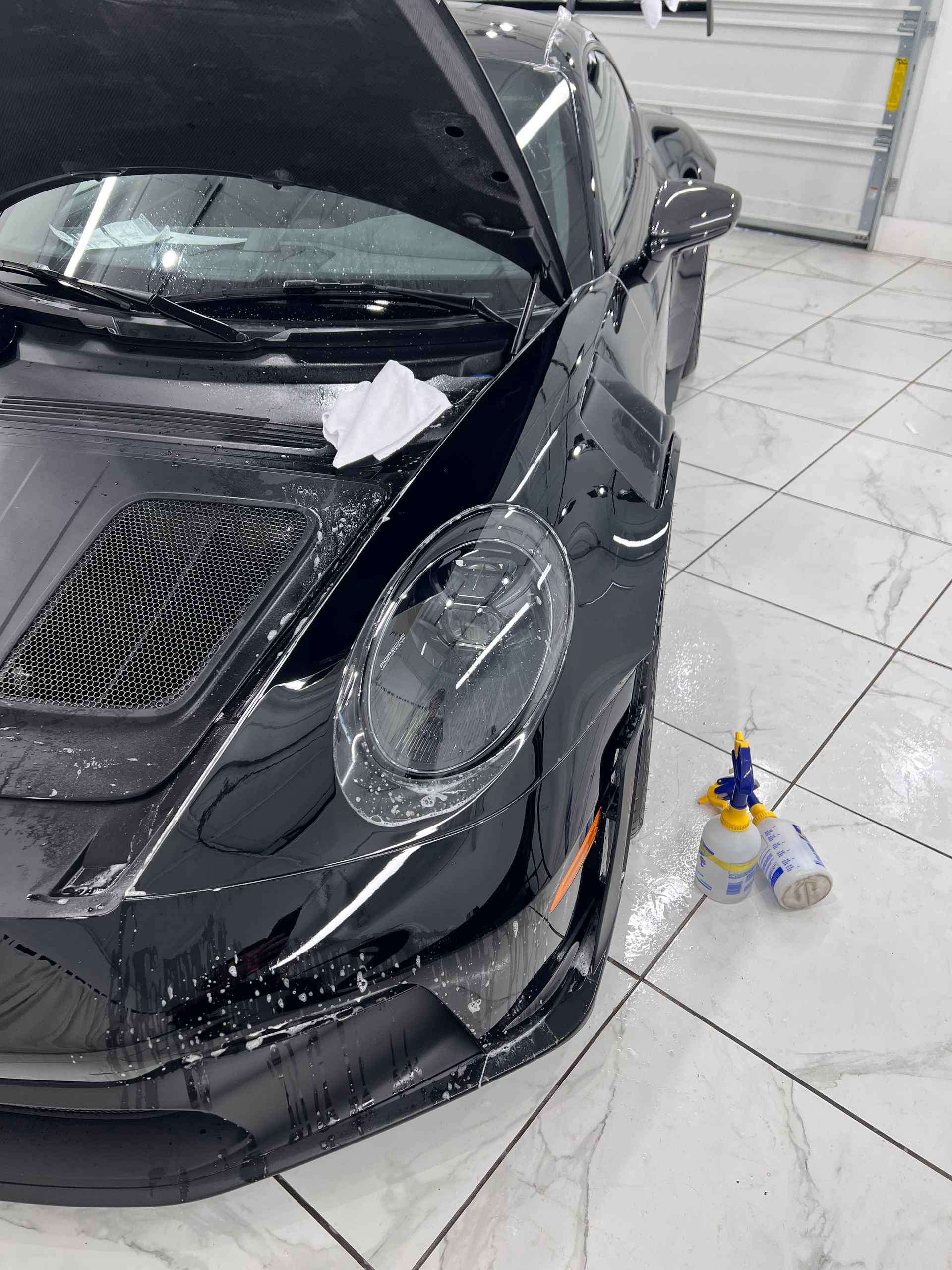 Black sports car with hood open, being worked on, in a garage.