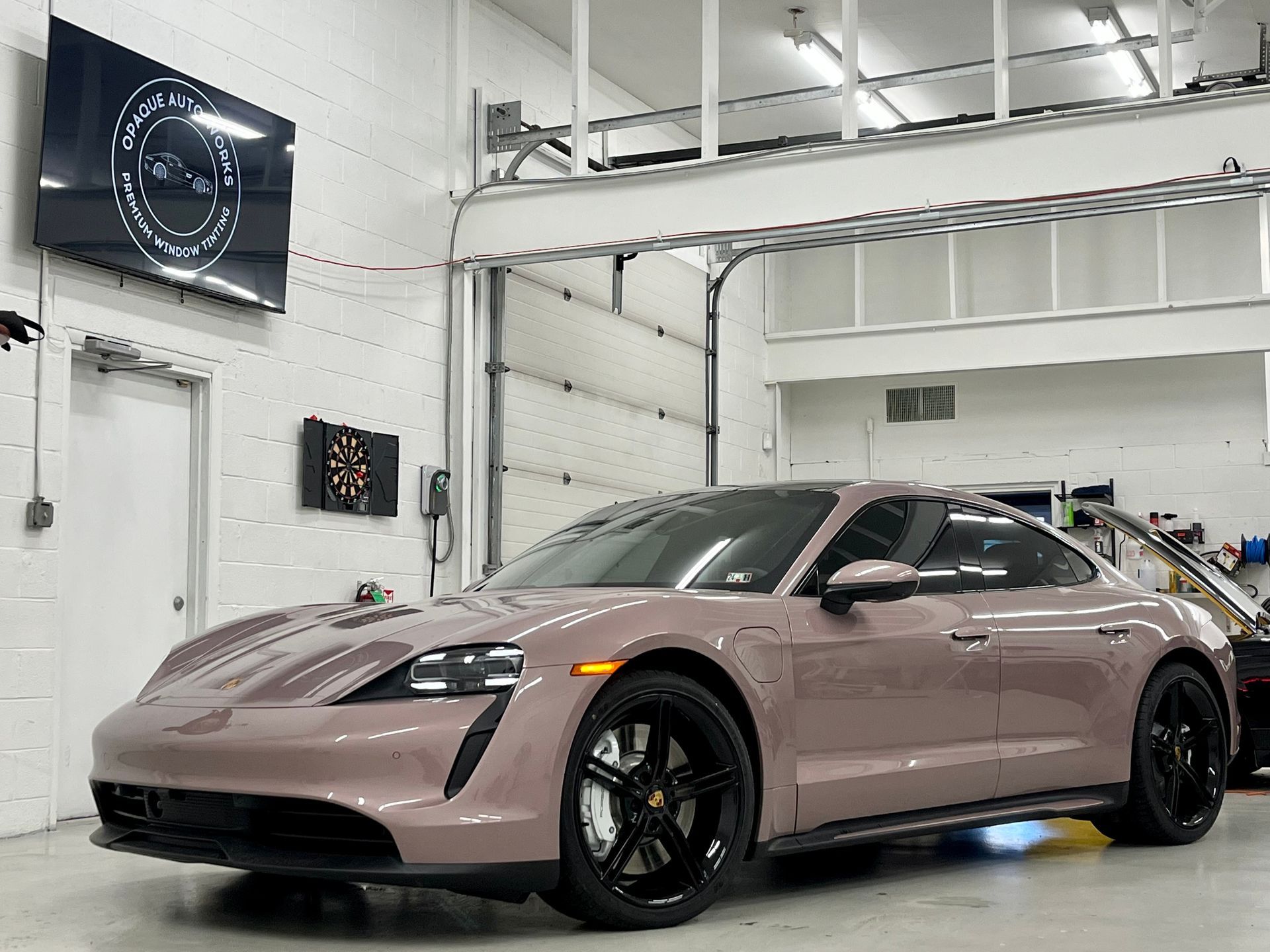 A mauve Porsche Taycan sports car in a garage with black rims and a partially open garage door.