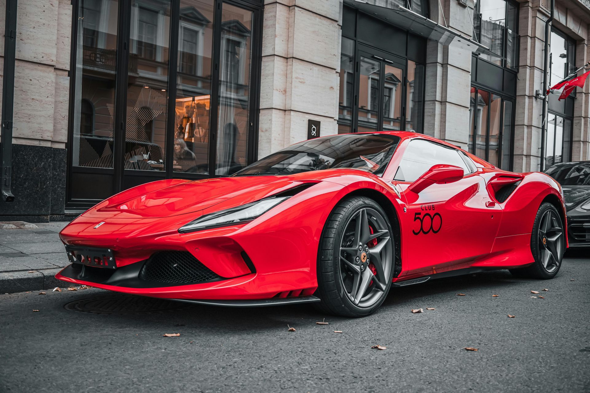 Red Ferrari sports car parked on a city street, in front of a building with shop windows.