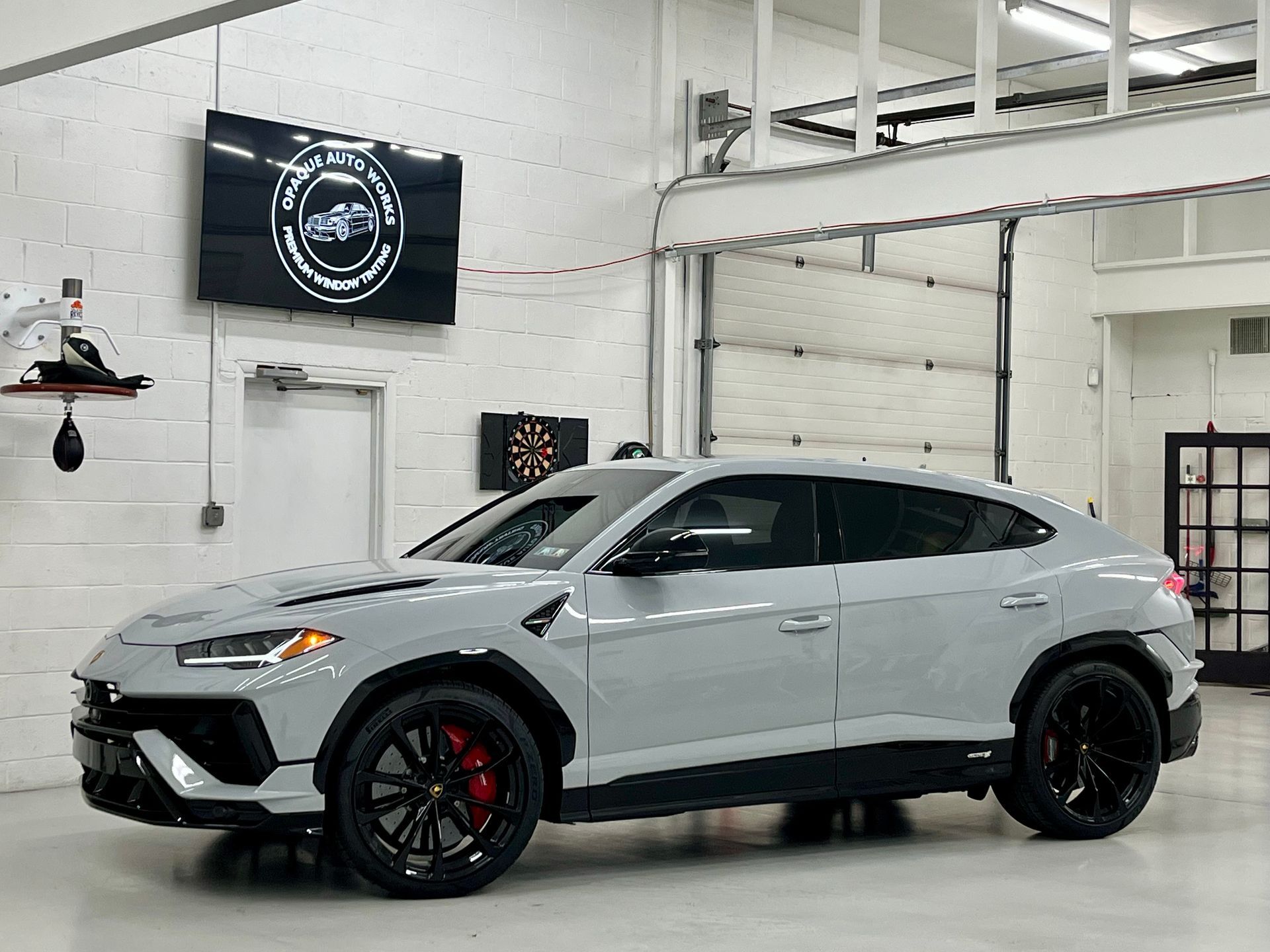 Silver sport SUV in a garage, with black wheels and red brake calipers, parked under white beams.