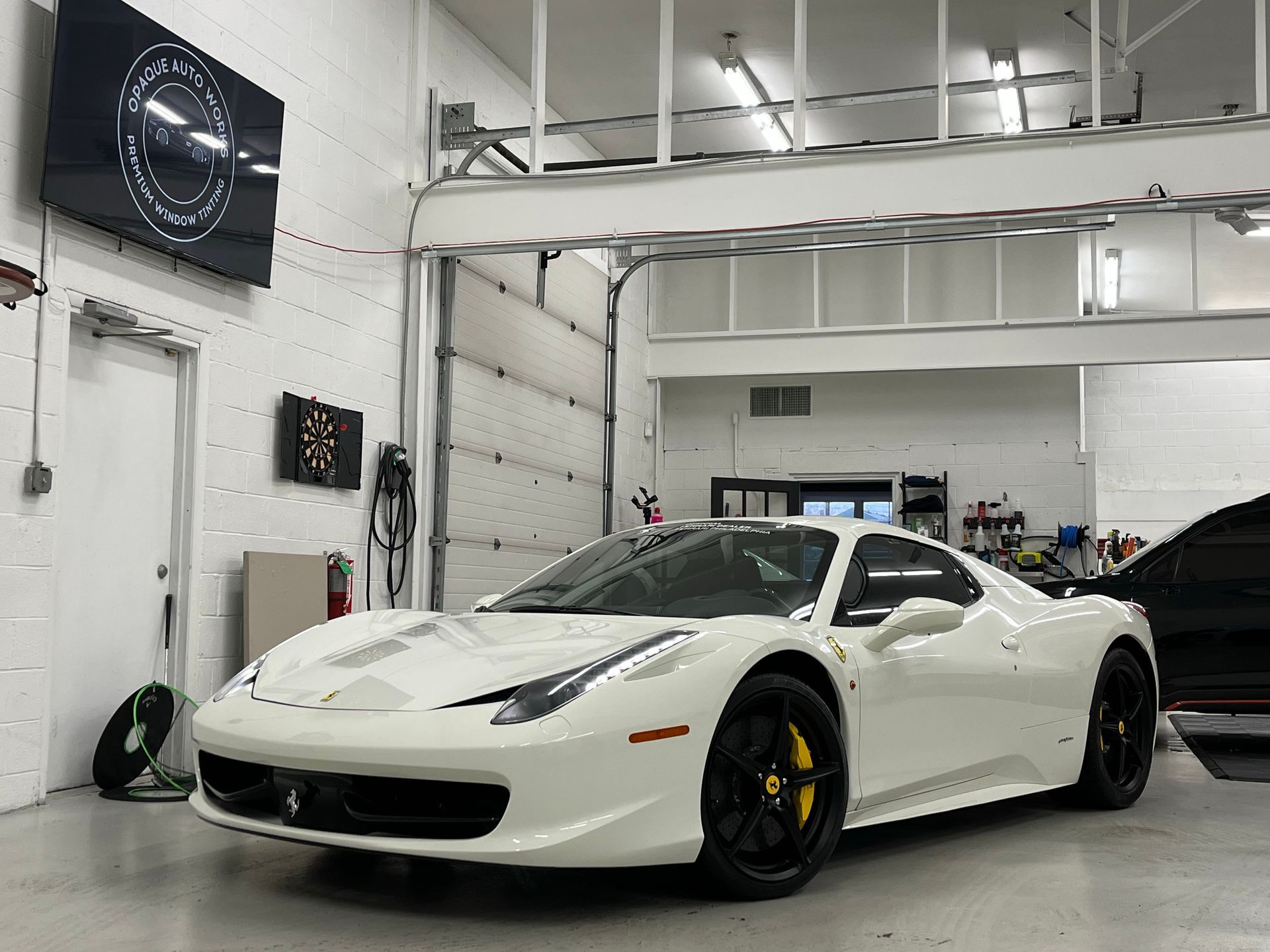 White sports car in a bright garage, parked at an angle with black wheels and yellow brake calipers