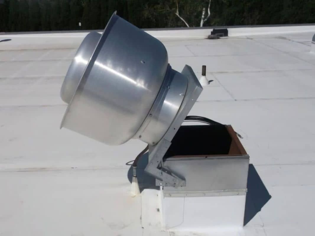 Hinged exhaust fan shown open for access A white roof with a hinged metal exhaust fan on it tilted open.
