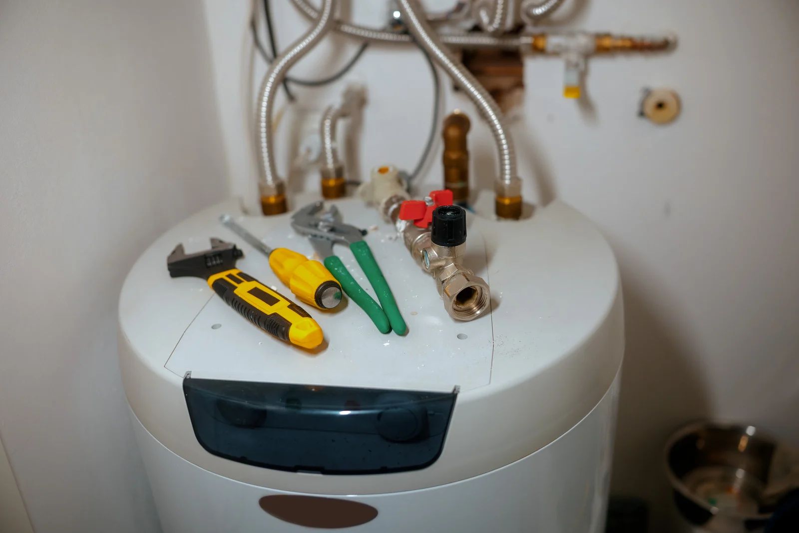 Hand tools and plumbing parts on top of a white water heater in a utility room