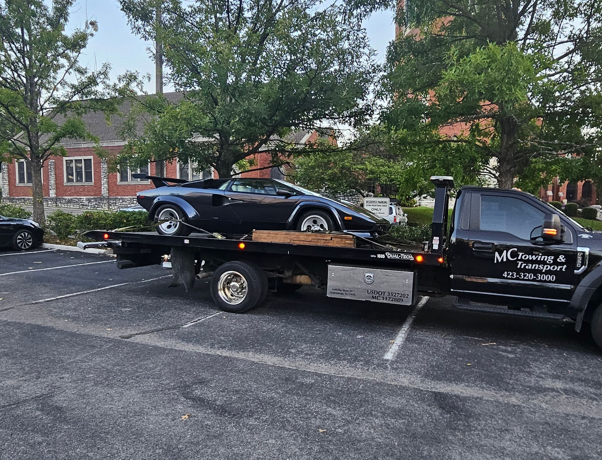 A black Lamborghini Countach loaded on a flatbed tow truck in a parking lot.